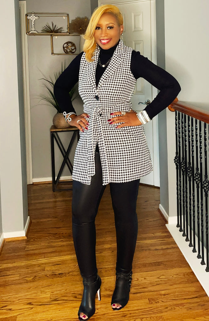 Black and white houndstooth sleeveless jacket, styled for fall with leggings and boots."