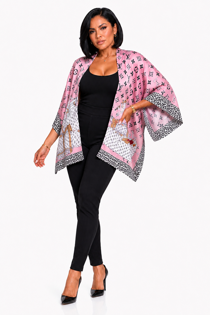 A woman modeling a pink open-front kimono-style cardigan with black and white monogram-like print and leopard-print wide sleeves, worn over a black bodysuit and black pants against a light gray studio background.