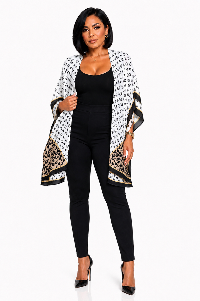 A woman modeling a black and white patterned open-front kimono jacket with leopard print panels and black high heels, worn over a black bodysuit and pants against a plain white studio background.
