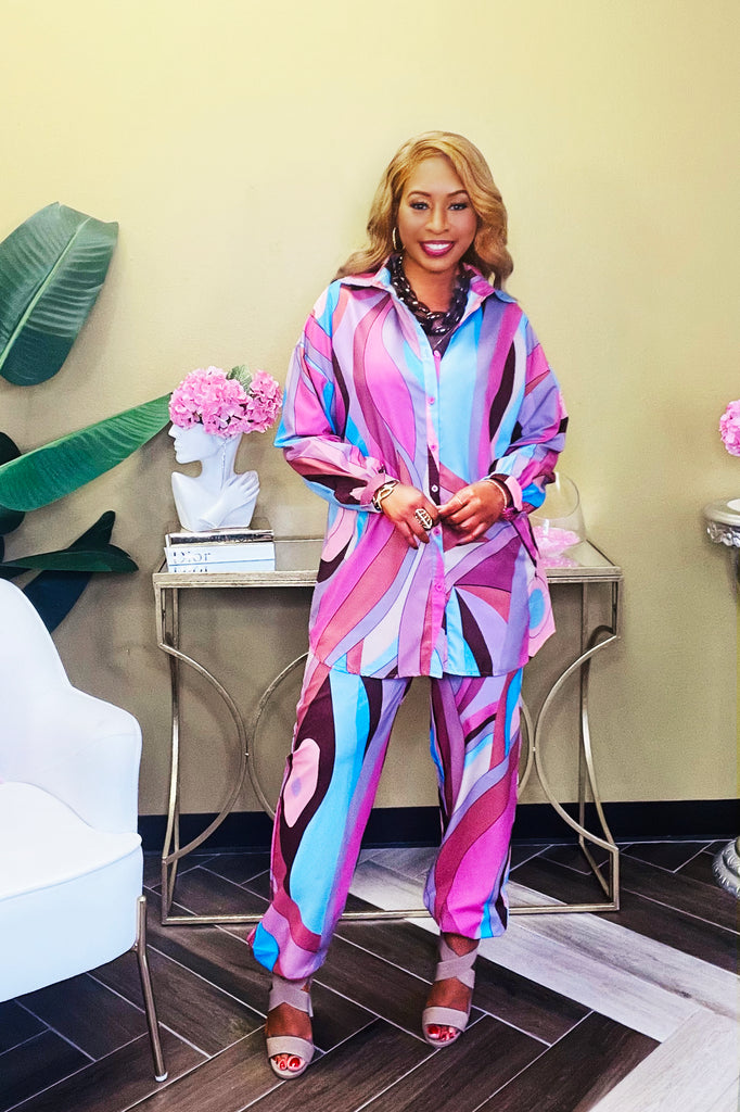 Woman wearing a pink multicolored pant set with a versatile fit—pants can be styled as joggers or loose slacks. Top includes fully functional side pockets. Model is 5'5" and 160 pounds, wearing a size medium.